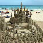 A sand castle with towers and a train track and sand trees