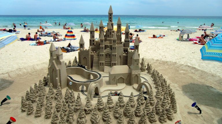 A sand castle with towers and a train track and sand trees